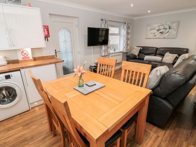 A dining area with wooden table and chairs next to a kitchen and living room with leather sofas at Cheviot View in Beadnell