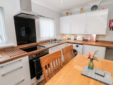 A kitchen with wooden countertops white cabinets a dining table with chairs and a flower in a vase at Cheviot View in Beadnell