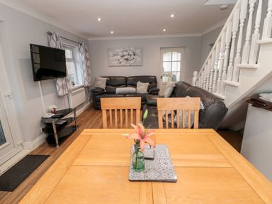A dining table with a flower vase in a living room with leather sofas a TV and stairs at Cheviot View in Beadnell