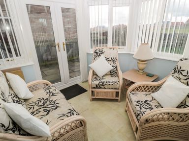 A sunroom with wicker furniture and a side table with a lamp at Cheviot View in Beadnell