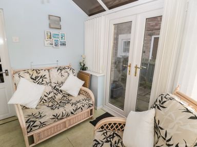 A sitting room with two cushioned rattan sofas white curtains and French doors at Cheviot View in Beadnell