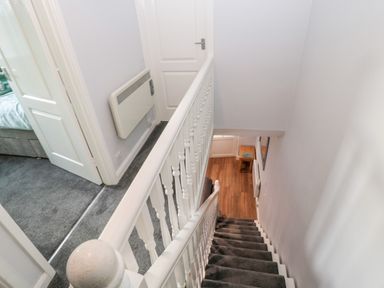 A staircase with gray carpet and white railing leading to a wooden floor hallway with a small table and a mirror at the bottom at Cheviot View Beadnell