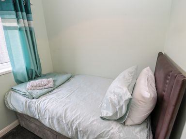 A small bedroom with a single bed a brown headboard and teal curtains at Cheviot View in Beadnell