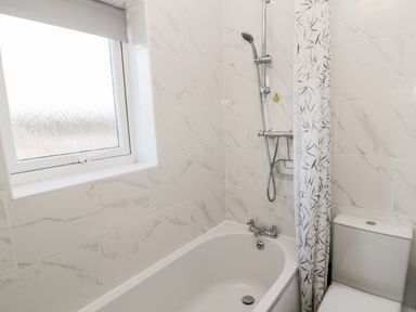 A bathroom with a bathtub shower combination next to a window and a toilet at Cheviot View in Beadnell