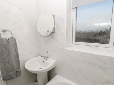 A bathroom with a sink a round mirror a window with frosted glass and a towel hanging on a towel ring at Cheviot View in Beadnell