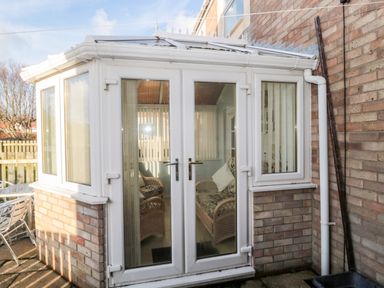A conservatory with glass doors and windows attached to a brick house with wicker furniture inside at Cheviot View in Beadnell