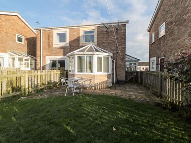 A backyard with grass patio table and chairs surrounded by wooden fences at Cheviot View in Beadnell