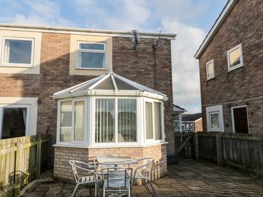 A small patio area with a table and four chairs outside a brick house with a white conservatory at Cheviot View in Beadnell