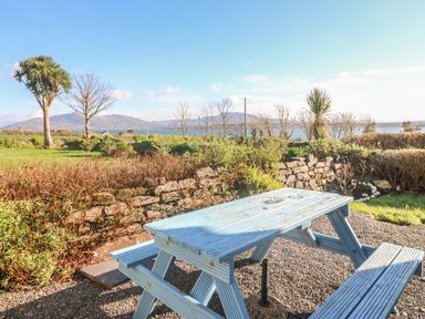An outdoor picnic table and benches on gravel with stone wall and mountain view at Kates Cottage in Knightstown Valentia Island County Kerry