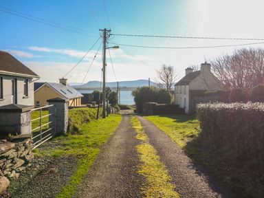 A narrow road with moss between houses and telephone poles near a body of water at Kates Cottage in Knightstown Valentia Island County Kerry