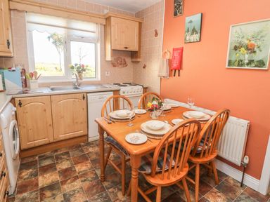 A kitchen with wooden cabinets a dining table set for four and an orange wall at Kates Cottage in Knightstown Valentia Island County Kerry