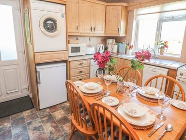 A kitchen with wooden cabinets a dining table set with plates glasses and cutlery and appliances at Kates Cottage in Knightstown Valentia Island County Kerry