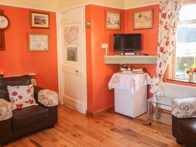A living room with two armchairs a small TV on a wall shelf and a window with floral curtains at Kates Cottage Knightstown Valentia Island County Kerry