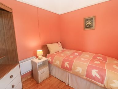 A small bedroom with a single bed a bedside table with a lamp a wooden wardrobe and a framed picture on the wall at Kates Cottage in Knightstown Valentia Island County Kerry