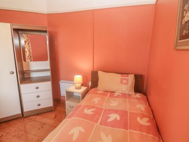 A bedroom with a single bed bedside table with a lamp and a wardrobe with mirror at Kates Cottage in Knightstown Valentia Island County Kerry