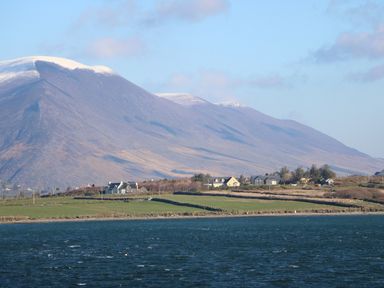 A body of water in front of green fields and houses with mountains in the background at Kates Cottage in Knightstown Valentia Island County Kerry