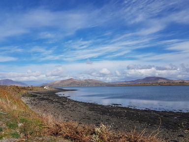 A coastal landscape with mountains in the background and a small white house near the shore at Kates Cottage in Knightstown Valentia Island County Kerry