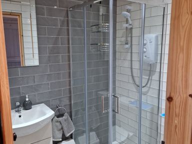 A bathroom with a glass shower enclosure a white sink with a soap dispenser and a striped hand towel at Kates Cottage Knightstown Valentia Island County Kerry