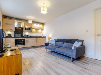 A kitchen with wooden cabinets and appliances next to a living area with a blue sofa and a wooden TV stand at Sunrise The Bay near Filey