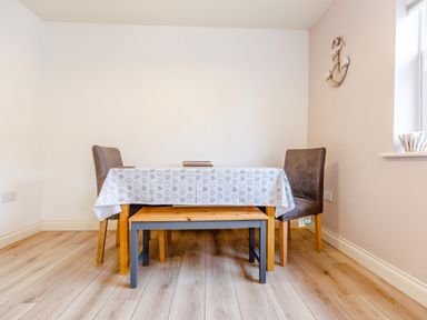 A dining area with a table covered by a heart patterned tablecloth two chairs and a bench on wooden flooring at Sunrise The Bay near Filey