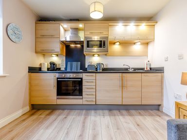 A kitchen with wooden cabinets black countertop oven microwave kettle toaster and sink at Sunrise The Bay near Filey