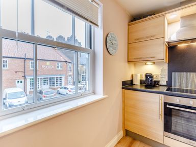 A kitchen corner with a window overlooking parked cars and a building with a bayside sign at Sunrise The Bay near Filey
