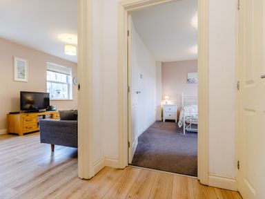 A hallway with doors leading to a bedroom with a bed and nightstand and a living room with a sofa and television at Sunrise The Bay near Filey