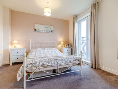 A bedroom with a white metal bed and two white bedside tables with lamps and a door with curtains at Sunrise The Bay near Filey