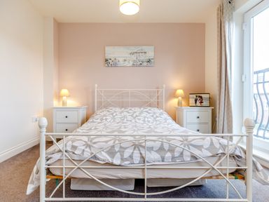 A bedroom with a metal bed frame two bedside tables with lamps and a painting on the wall at Sunrise The Bay near Filey