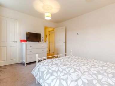 A bedroom with a bed a white dresser a television and two doors at Sunrise The Bay near Filey