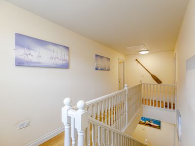 A hallway with white wooden railing paintings on the walls and a wooden paddle mounted on the wall at Sunrise The Bay near Filey