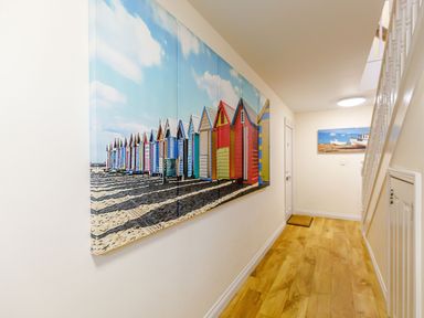 A hallway with wooden floor and wall art of colorful beach huts and boats at Sunrise The Bay near Filey