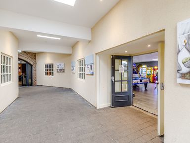 A corridor with paintings on walls and a door leading to an arcade room at Sunrise The Bay near Filey