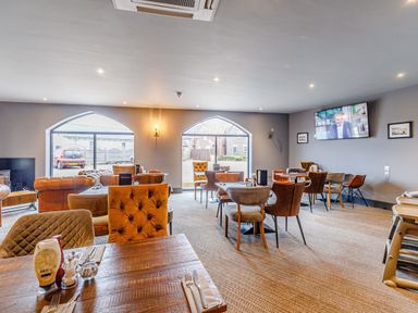 A dining area with tables and chairs a television on the wall and windows overlooking a parking area at Sunrise The Bay near Filey