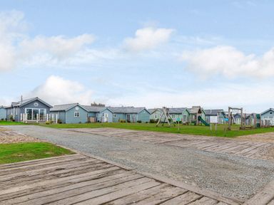 A gravel road with wooden boards alongside blue cottages and a playground at Sunrise The Bay near Filey