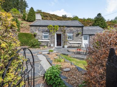 A stone cottage with slate roof and a garden pathway leading to the entrance at Henrhiw Bach in Penmachno
