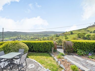 A garden patio with a glass table and chairs overlooking green hills at Henrhiw Bach in Penmachno