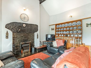A living room with black leather sofas a fireplace and a wooden plate rack with blue and white plates at Henrhiw Bach in Penmachno