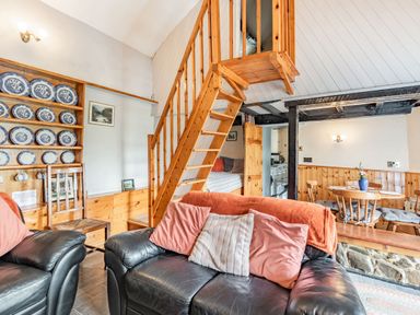 A living room with black leather sofas and wooden staircase next to a dining area with wooden table and chairs at Henrhiw Bach in Penmachno
