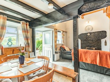 A dining area with a round wooden table and chairs next to a living room with black leather sofas and a fireplace at Henrhiw Bach in Penmachno