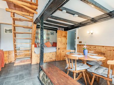 A dining area with a wooden table and cushioned chairs next to a wooden staircase and a seating nook at Henrhiw Bach in Penmachno