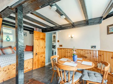 A dining area with a round wooden table and four chairs with cushions and a built-in wooden bench with cushions at Henrhiw Bach in Penmachno