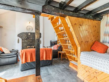 A living room with wooden stairs a black leather sofa and a gray tiled floor at Henrhiw Bach in Penmachno