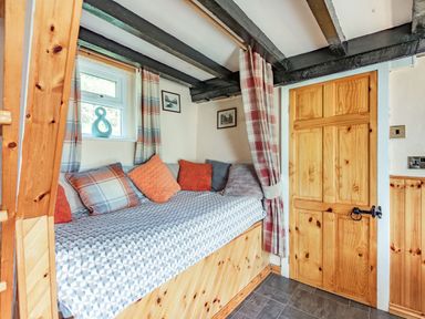 A small room with a daybed with cushions next to a window and a wooden door with black hinges and a latch at Henrhiw Bach in Penmachno