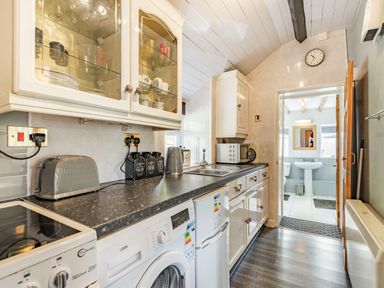 A kitchen with white cabinets black countertop washing machine toaster and kettle leading to a bathroom at Henrhiw Bach in Penmachno