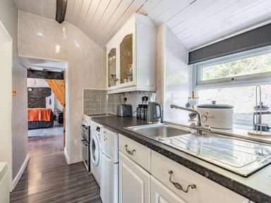 A kitchen with a sink a washing machine a kettle and a bread box next to a window at Henrhiw Bach in Penmachno