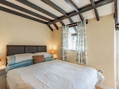 A bedroom with a double bed bedside tables lamps window with patterned curtains and exposed ceiling beams at Henrhiw Bach in Penmachno