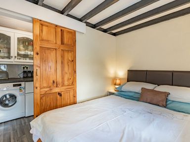 A bedroom with a bed a bedside table with a lamp a wooden sliding door opening to a small kitchen with washing machine at Henrhiw Bach in Penmachno