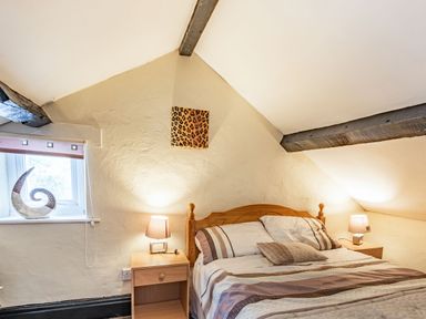 A bedroom with a double bed bedside tables and lamps under a sloped ceiling at Henrhiw Bach in Penmachno