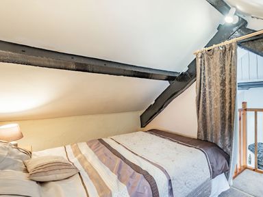A bedroom with a double bed and striped bedding under a sloped ceiling with exposed beams at Henrhiw Bach in Penmachno